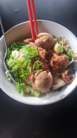 Téléchargez les photos : Un bol appétissant de délices culinaires asiatiques avec des poireaux salés et de succulentes boulettes de viande, accompagnées de baguettes, reposant sur une table bien dressée - en image libre de droit