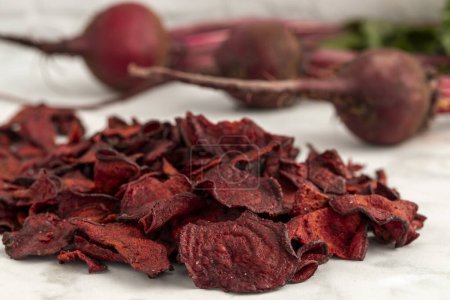 Photo for Close up of red beet plant based chips with sea salt sitting in a pile on marble kitchen counter with fresh beet roots in the background - Royalty Free Image