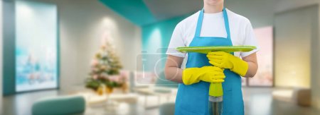 Photo for A cleaning lady with a mop stands against the backdrop of decorating for the New Year premises. - Royalty Free Image