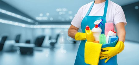 Téléchargez les photos : Une femme de ménage se tient debout avec un seau et des produits de nettoyage sur un fond flou. - en image libre de droit