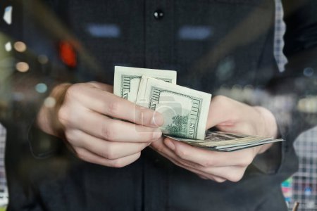 Téléchargez les photos : A man counts dollars closeup on a blurred background. - en image libre de droit