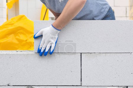 Téléchargez les photos : Un travailleur pose un bloc de gaz sur le mur. Concept de construction de maison. - en image libre de droit