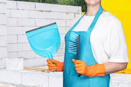 Photo for The cleaning lady shows a broom and a dustpan in the background of a construction site. - Royalty Free Image