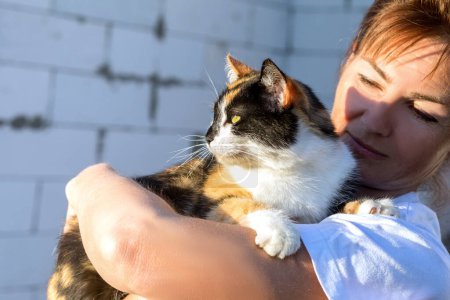 Foto de Una mujer sostiene un gato mascota contra el fondo de una casa construida. - Imagen libre de derechos