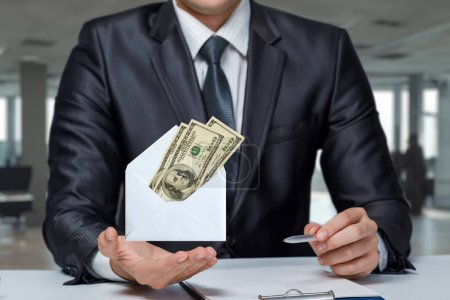 Téléchargez les photos : Un homme d'affaires montre une enveloppe avec des dollars sur un fond de bureau flou. - en image libre de droit