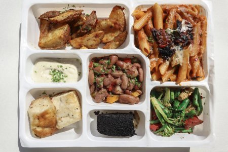 Photo for Continental lunch box consists of Potato wedges, Pasta, Brocolli salad, bun, sauce Beans and brownie - Royalty Free Image