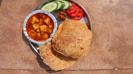 Leckeres Bedmi Puri mit Aloo ki sabzi in einer Schüssel serviert. Puri bhaji serviert mit Gurkensalat, Tomate mit würziger Essiggurke