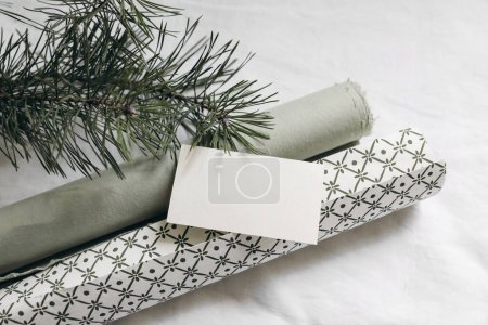 Photo for Christmas still life. Blank business card, invitation mockup. Green gift wrapping papers and pine tree branches on white linen tablecloth. Winter festive flat lay, top view, festive still life, decor - Royalty Free Image