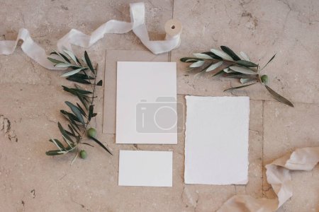 Photo for Summer wedding stationery set, suite. Italian, Greek mock-up scene with blank paper greeting cards, envelope on beige marble tiles background. Green olive tree branches, silk ribbon, flat lay, top. - Royalty Free Image
