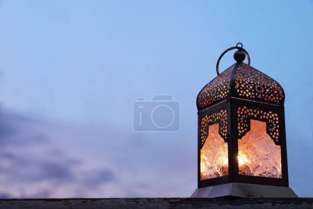 Photo for Close-up of dark silhouette of glowing ornamental Moroccan lantern. Blurred evening sky, dusk. Festive still life for muslim holiday Ramadan Kareem. Eid ul Fitr, Eid al Adha, Iftar dinner. Copy space. - Royalty Free Image