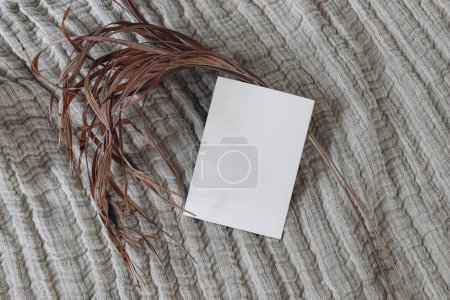 Photo for Tropical boho still life. Blank greeting card mockup and dry palm leaf on beige linen muslin throw, blanket. Summer stationery template, design. Boho wedding invitation, flat lay, top view, no people. - Royalty Free Image