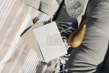 Summer vacation still life. Closeup of blank greeting card, invitation mockup. Beige striped beach towel. Sun bed composition with fresh pear fruit in sunlight, long shadows. Elegant stationery, top