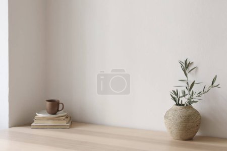 Photo for Neutral Mediterranean home design. Textured vase with olive tree branches, cup of coffee. Books on wooden table. Living room still life. Empty wall copy space. Modern interior, no people, lateral view - Royalty Free Image
