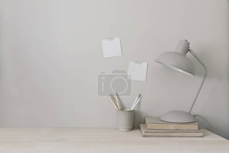 Photo for Wooden desk with lamp, books and cup holder for pencils. Note pad mockups taped on wall. Neutral stylish minimal workspace. Beige background, empty copy space. Home office concept. Lifestyle banner. - Royalty Free Image