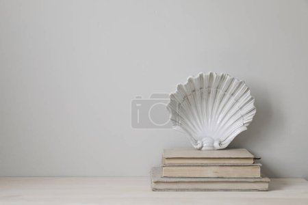 Photo for Stylish white vintage ceramic plate in shape of seashell on old books. Closeup of elegant wooden table. Empty beige wall background, nobody. Summer vacation marine design, classic artistic decoration. - Royalty Free Image