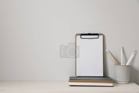 Photo for Wooden clipboard mockup with notebooks and pencils holder on a wooden table. Home office, creative desk with office supplies and beige wall space, elegant minimal interior, home decor. Nobody. - Royalty Free Image