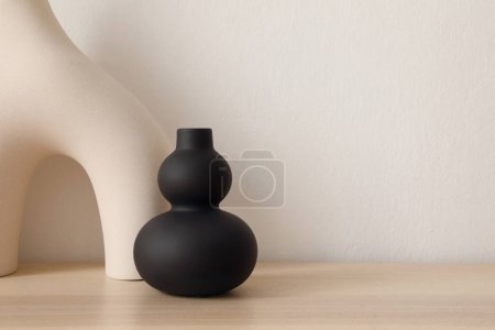 Photo for Set of modern ceramic vases of geometric organic shape on wooden table. Modern black sculpture. Beige wall. Abstract trendy artistic background. Web banner. - Royalty Free Image