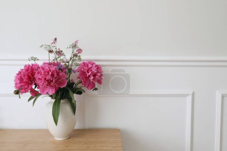 Photo for Beautiful floral bouquet. Vase with pink peonies flowers on ooden table, desk. White wall background with elegant moulding. Wedding or birthday concept, elegant interior still life, web banner. - Royalty Free Image