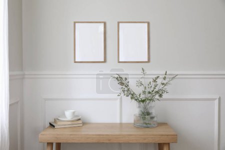 Photo for Two empty vertical picture frame mockups hanging on wall. Cup of coffee, books. Wooden desk, table. Vase, green grasses and cow parsley. Minimal working space, home office, elegant Scandi interior. - Royalty Free Image