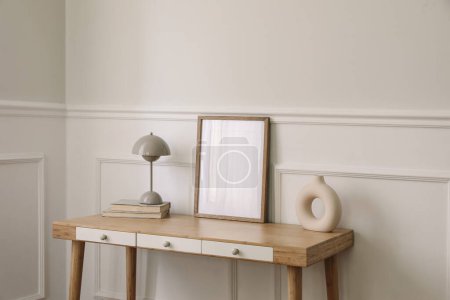 Photo for Modern living room, home office. Trendy round vase, beige lamp and old books. Blank picture frame mockup. Bamboo table with white drawers. Minimal Scandi boho interior, home, beige wall background. - Royalty Free Image