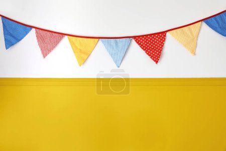 Photo for Hanging colorful bunting flags on white wall background. Yellow festive web banner. Festa Junina holiday, June Festival celebration concept. Decoration for birthday party, decorative Midsummer frame. - Royalty Free Image