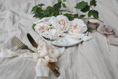 Photo for Elegant wedding still life, tableware set. Plate, golden cutlery, delicate pink nude colored roses. Beige linen tablecloth. Blurred background, selective focus, festive feminine table setting, ribbons - Royalty Free Image