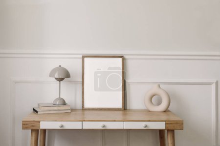 Photo for Elegant living room, home office. Modern round vase, beige lamp and old books. Blank wooden picture frame mockup. Bamboo table with white drawers, Scandi boho interior, home. Beige wall background. - Royalty Free Image