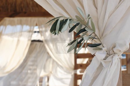 Photo for Closeup of green olive tree branch, blurred organza veils. White beach canopies, chuppah. Luxury beach tents at resort, gazebo. Mediterranean outdoor wedding concept, summer birthday party, vacation. - Royalty Free Image