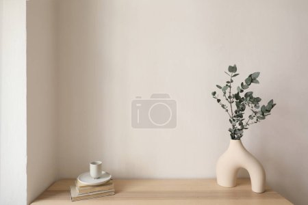 Photo for Eucalyptus tree branch in modern organic vase. Cup of coffee, old books on wooden table. Empty beige wall mockup, copy space. Elegant living room, Scandinavian minimalist interior, home, no people. - Royalty Free Image