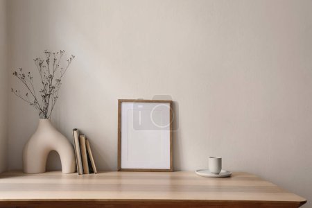 Photo for Elegant scandinavian interior, living room. Blank wooden picture frame mockup on table. Modern vase, dry flowers and cup of coffee, tea. Trendy working space, home office, beige wall background. - Royalty Free Image