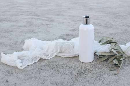 Photo for White cosmetic plastic bottle mockup with green olive tree branch and muslin veil. Natural liquid soap, shampoo or moisturizer. Grey grunge concrete floor background. Summer skin care. Cosmetology. - Royalty Free Image