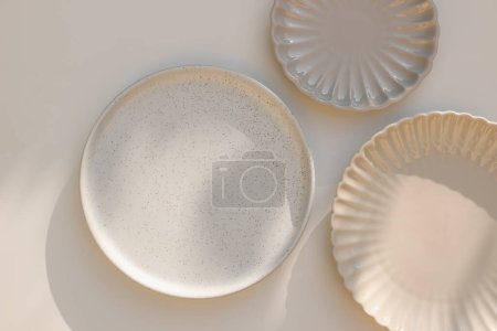Photo for Three different size stoneware plates on beige table background. Flat lay, top view. Natural color disgware. Textured grainy pattern and scallop shaped plates. Ceramics. Kitchen, restaurant concept - Royalty Free Image