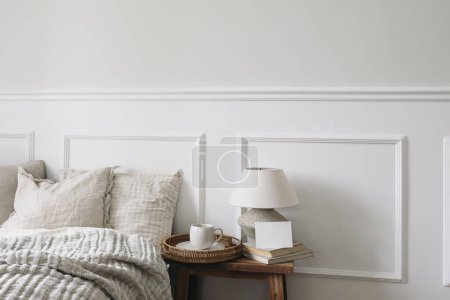 Photo for Blank greeting card, invitation mockup. Breakfast in bed concept. Cup of coffee, table lamp with linen shade, vintage wooden night stand. Linen beddings, elegant classic bedroom interior. White wall. - Royalty Free Image