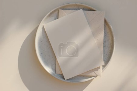 Photo for Summer minimal wedding stationery. Blank vertical greeting card mockup with beige envelope, invitation. Ceramic dessert plate in golden sunlight. Table background with shadows overlay, flatlay, top - Royalty Free Image