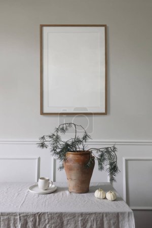Photo for Elegant interior, Christmas table setting decor. Winter art composition. Blank wooden picture frame mockup hanging on beige wall. Pine tree branches in vase. Cup of coffee, white pumpkins, vertical. - Royalty Free Image