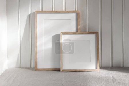 Set of blank vertical and square wooden picture frame mock ups in sunlight. White beadboard wainscot wall paneling background with shadows. Neutral Scandinavian home decor, nordic interior.