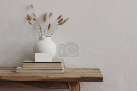 Photo for Blank business card mockup on old books. Modern round ceramic vase with dry bunny tails, Lagurus ovatus grass on wooden table, bench.. White wall background. Scandinavian interior. Home office. - Royalty Free Image