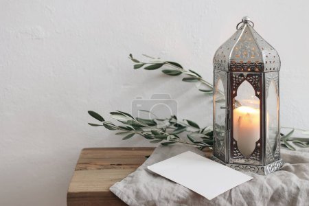 Photo for Ramadan Kareem holiday still life. Ornamental silver Moroccan lantern with olive tree branches. Blank greeting card, invitation mockup on wooden table, bench, blurred white wall background. - Royalty Free Image
