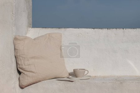 Photo for Summer vacation still life, relaxation concept. Mediterranean outdoor sitting area. Bench with beige waffle textured cushion. Cup of coffee. White wall background. Blue sky. Travel banner - Royalty Free Image