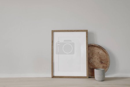 Photo for Blank vertical picture frame mockup. Poster display. Round wooden tray, concrete candleholder on working table, desk. Minimal rustic home. Scandinavian interior. White wall background, no people - Royalty Free Image