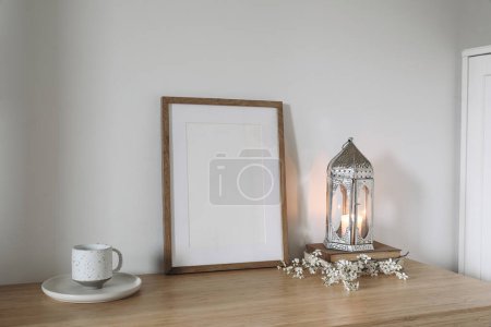 Photo for Silver Moroccan lantern, cup of tea, coffee on table. Wooden picture frame, poster mockup. White flowers, blooming prunus tree branches. White wall background, elegant interior, Ramadan Kareem - Royalty Free Image