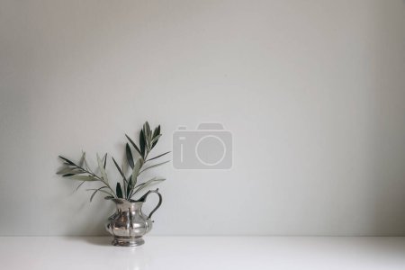 Photo for Olive tree branches, twigs in silver jug vase on white table. Empty mint green wall mockup, background. Working space, home office decor, vintage Mediterranean summer interior still life. - Royalty Free Image