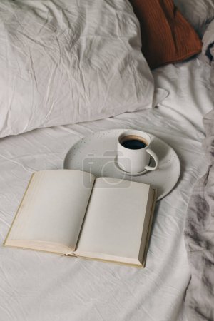 Photo for Cup of coffee, espresso. Open book, diary mockup on white bed sheet. Breakfast in bed concept. Blurred muslin, linen pillows, blanket. Scandinavian bedroom. Vertical top view, lifestyle banner. - Royalty Free Image