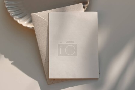 Photo for Summer neutral wedding stationery. Closeup of blank greeting card, envelope mockup in sunlight. Invitation, template. Beige dinner plate. Table background, shadows, elegant composition. Flatlay, top - Royalty Free Image