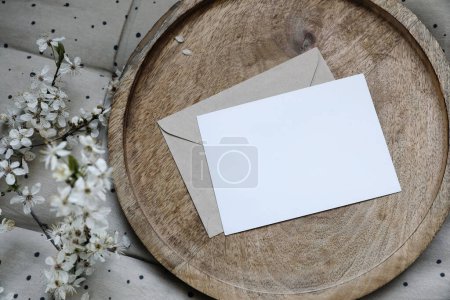 Photo for Spring still life composition. Blank greeting card mockup, craft envelope. Feminine styled photo. Floral scene. Blurred white cherry tree blossoms on wooden tray, polka dot beige seat cushion, topper. - Royalty Free Image