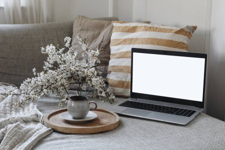Photo for Modern spring scandinavian living room interior. Sofa with linen yellow striped cushions and cup of coffee. Cherry plum blossoms in vase. Laptop mockup with blank screen, elegant home office decor. - Royalty Free Image