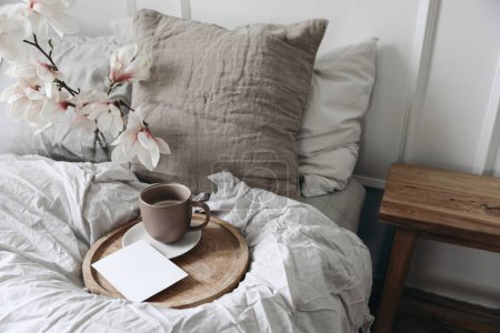 Photo for Breakfast in bed concept. Cup of coffee on wooden tray. Blank greeting card, invitation mockup. Bedroom view. Blurred beige linen pillows, blanket. Blooming magnolia branches in vase, top view. - Royalty Free Image
