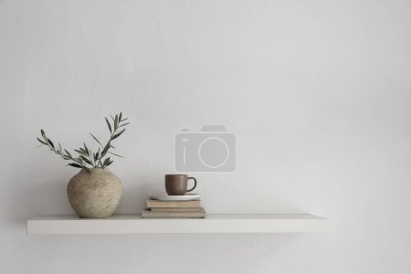 Photo for Elegant home still life. Floating shelf. Textured vase with green olive tree branches and old books. Cup of coffee, tea. Modern Mediterranean appartement. White wall background, interior indoor mockup - Royalty Free Image