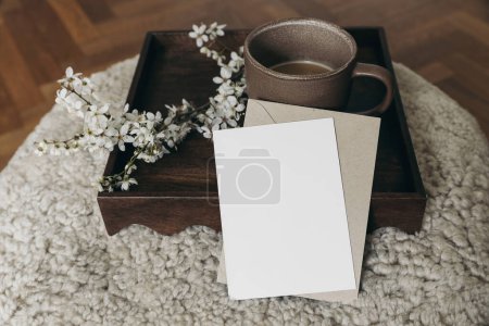 Photo for Spring Easter still life. Greeting card, envelope mockup. Cup of coffee. Feminine photo. Floral scene. Blurred cherry tree blossoms on wool taburet, stool, defocused wooden parquet floor. Front view. - Royalty Free Image