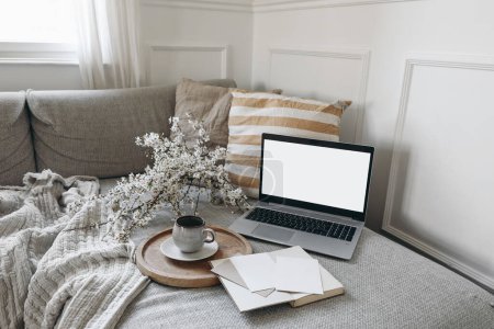 Photo for Spring scandinavian living room interior. Sofa with linen yellow striped cushions. Cup of coffee. Cherry plum blossoms in vase. Laptop mockup with blank screen and greeting cards, open book, home - Royalty Free Image